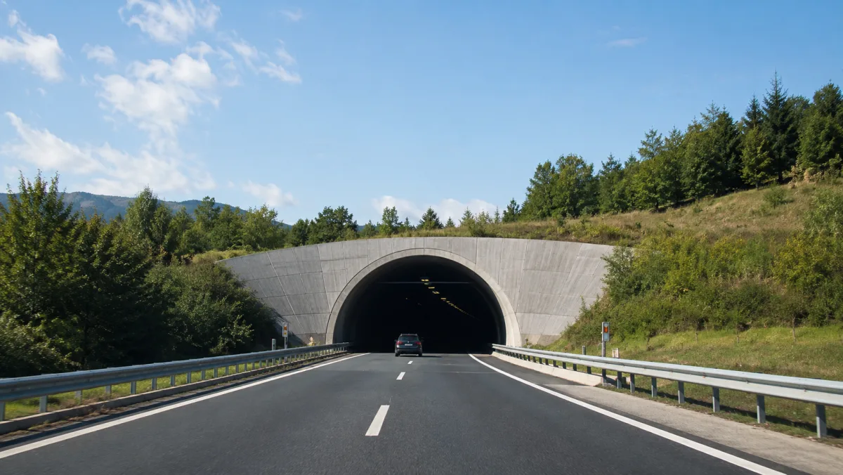 Un auto acercándose a la entrada de un túnel de carretera, donde el cielo abierto desaparece y las señales satelitales GPS quedan bloqueadas: la zona muerta donde los receptores congelan la última velocidad o cambian a navegación inercial por sensores de movimiento.