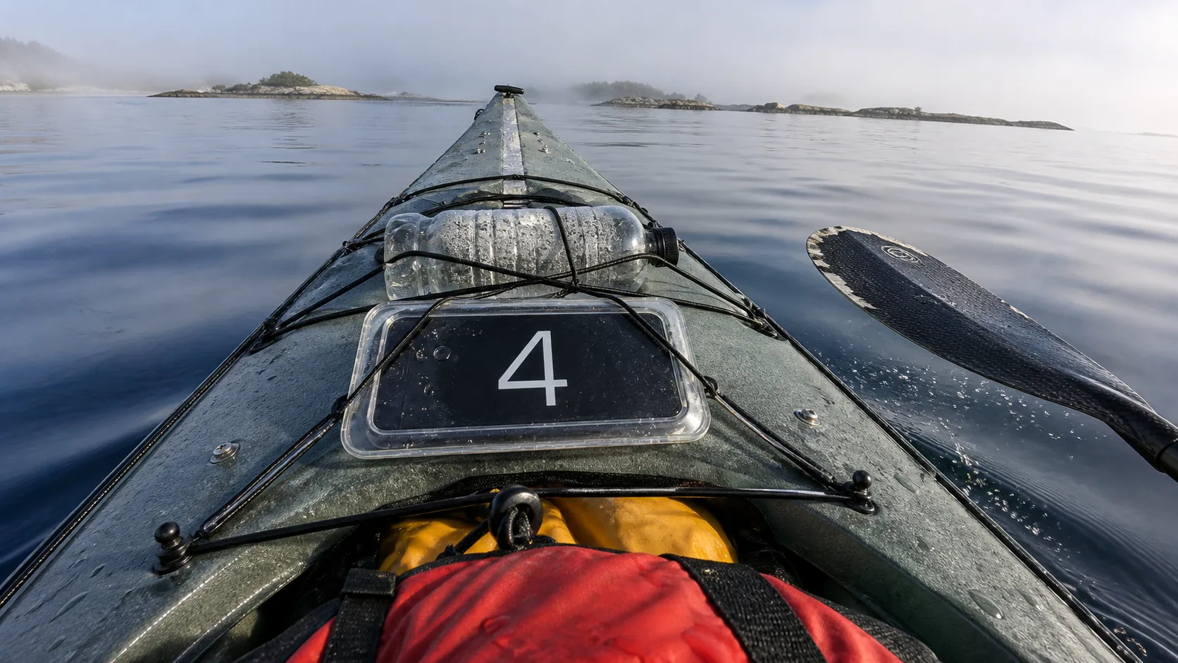 Sea kayak foredeck on a calm misty morning with GPS Speedometer in a clear waterproof case bungeed under the deck rigging