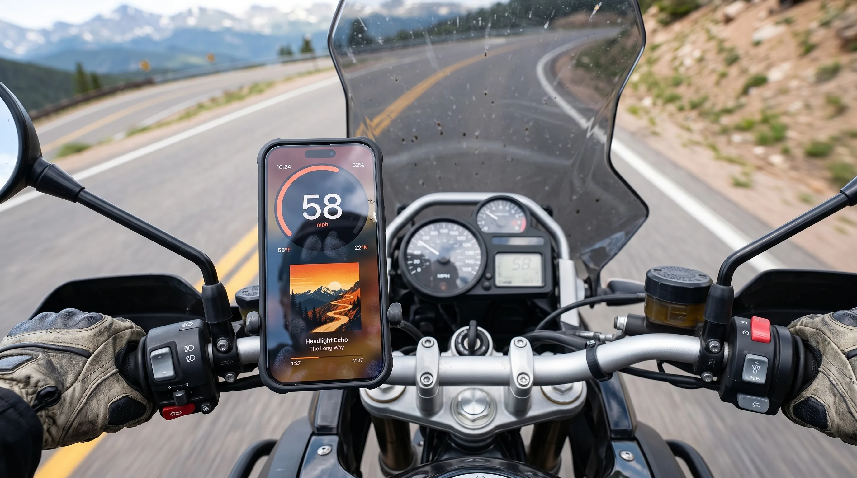 GPS Speedometer running on an iPhone in a vibration-damping handlebar mount on an adventure-touring motorcycle, scenic mountain road extending ahead
