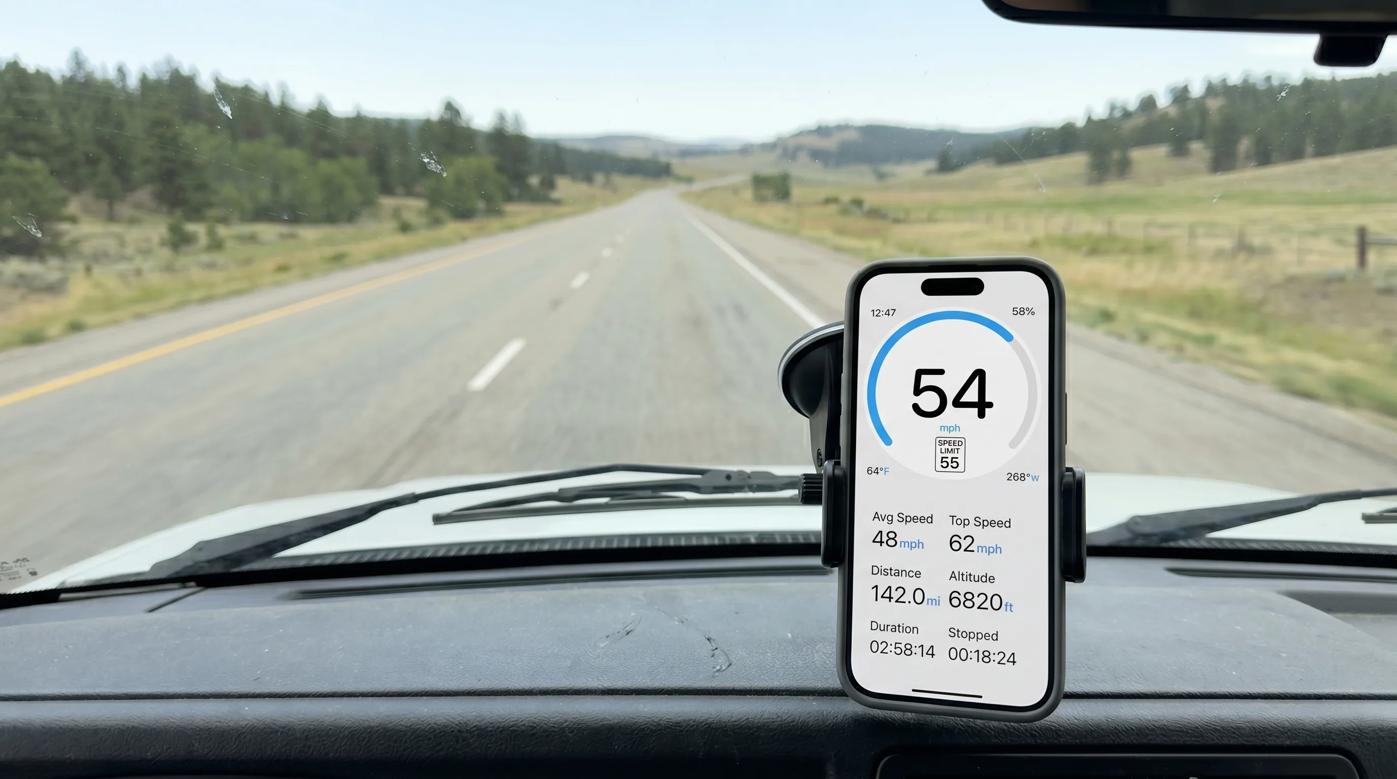 Wohnmobil-Cockpit mit auf dem Armaturenbrett montiertem iPhone, das GPS Speedometer zeigt — Blick durch die breite Windschutzscheibe auf eine zweispurige Landstraße in offener Landschaft
